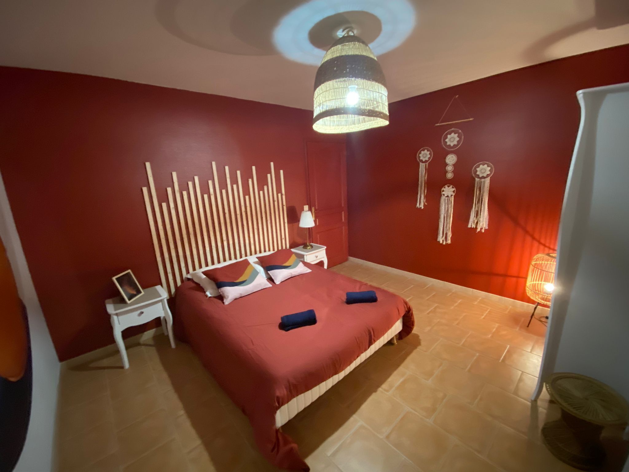 Quarto com cama, mesa de cabeceira, luminária e decorações nas paredes.