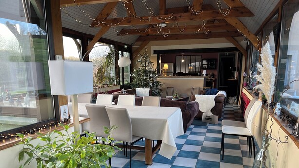 Un espace intérieur accueillant, aménagé avec des tables et des chaises, un sol à carreaux et un sapin de Noël.