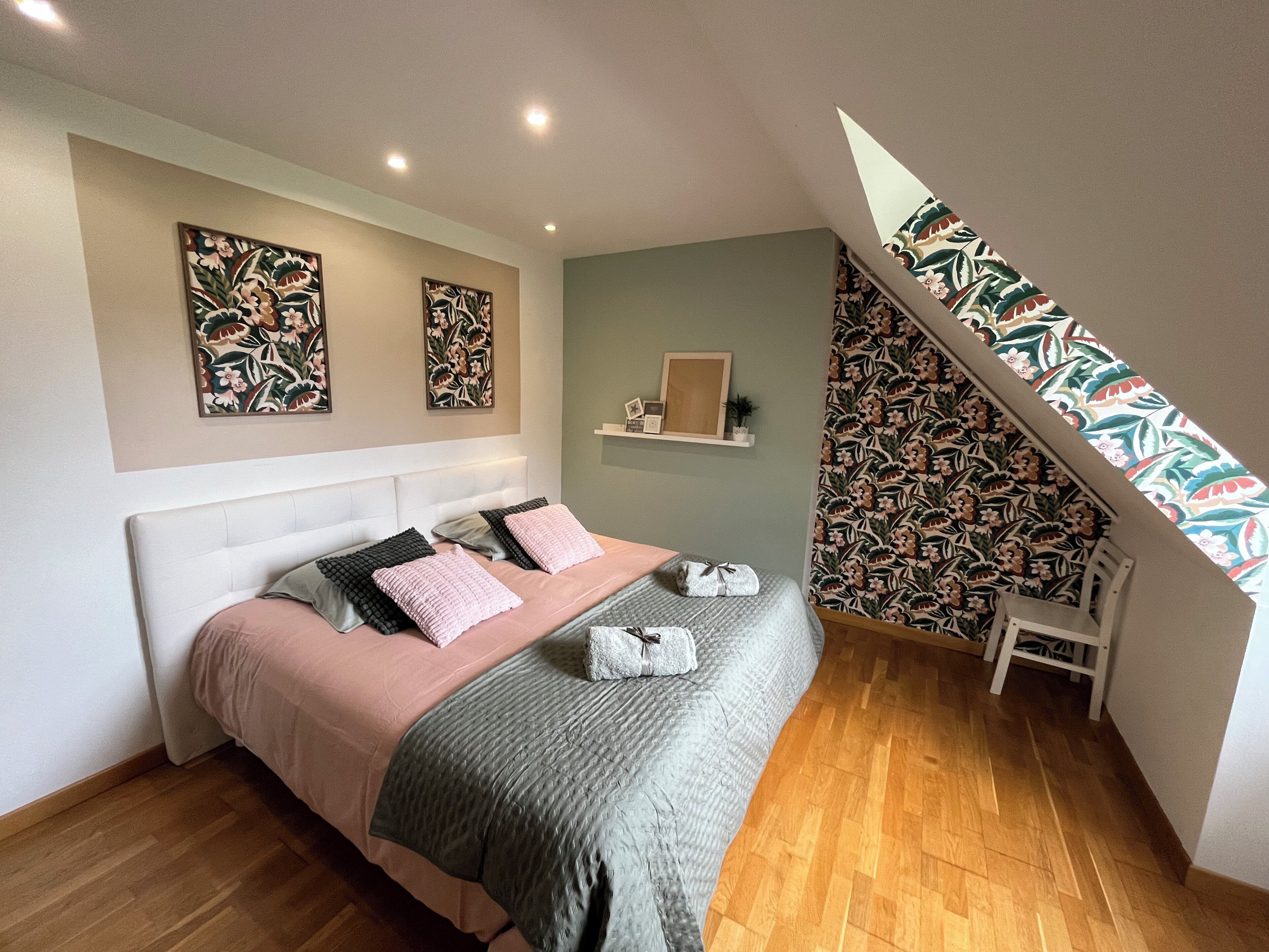 A bedroom with a bed, a wooden floor, a headboard, a shelf with a picture frame, and a patterned wall.