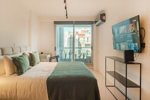 A modern hotel room with a bed, a TV on a stand, a balcony with a view of buildings, and a desk with a chair. - Unico Torre Lujo Deco Recoleta D901 (Buenos Aires)