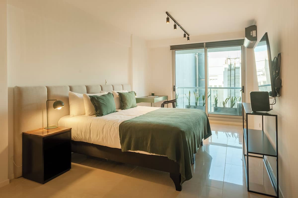 A modern bedroom with a bed, bedside tables, a desk, and a large window with a view.