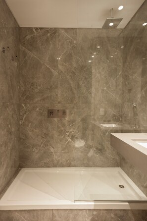 A modern bathroom with a glass-enclosed shower, marble walls, and a white sink. - Unico Torre Lujo Deco Recoleta D901 (Buenos Aires)