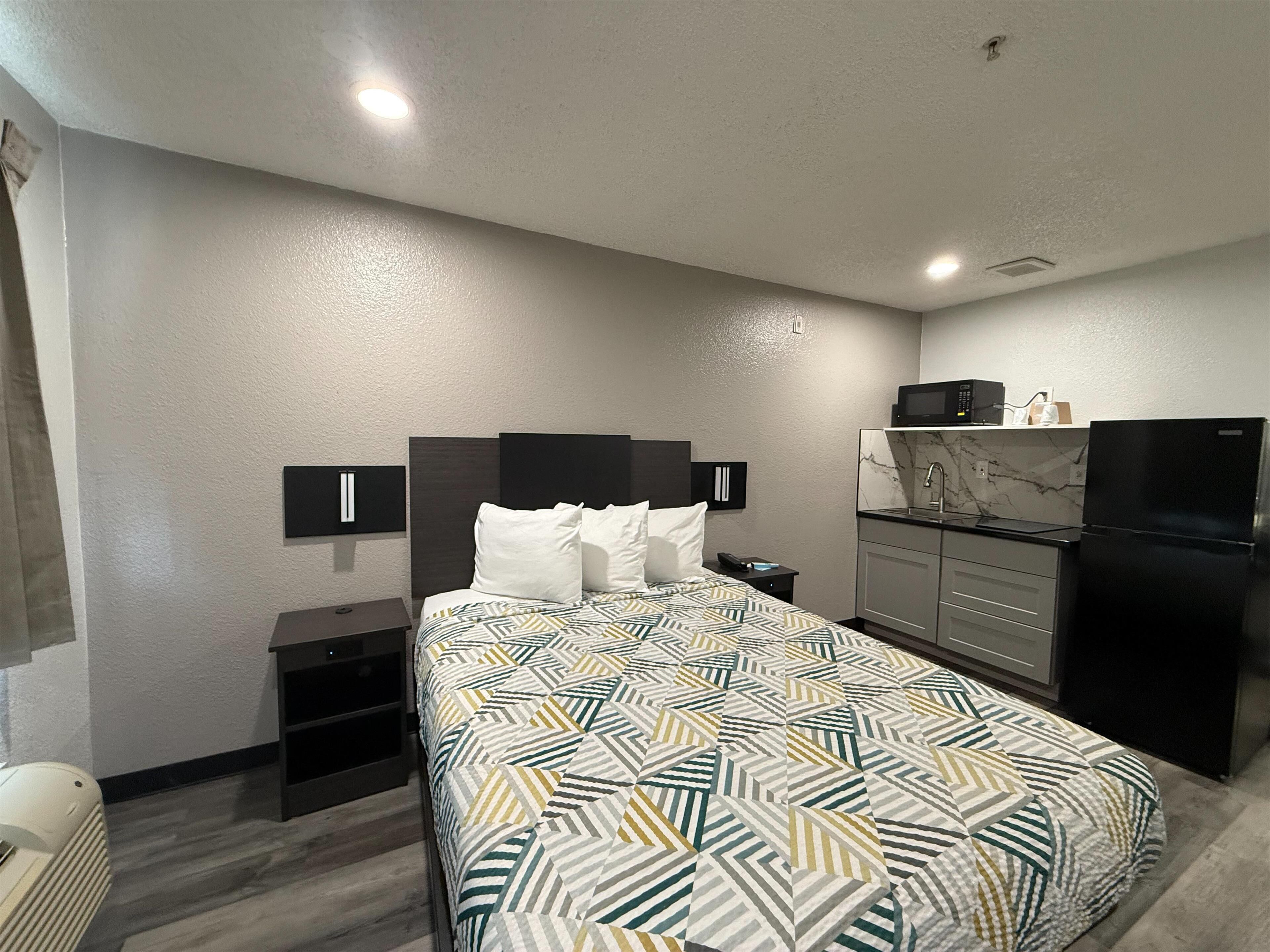 A hotel room with a bed, a small desk, a microwave, a refrigerator, and a sink.
