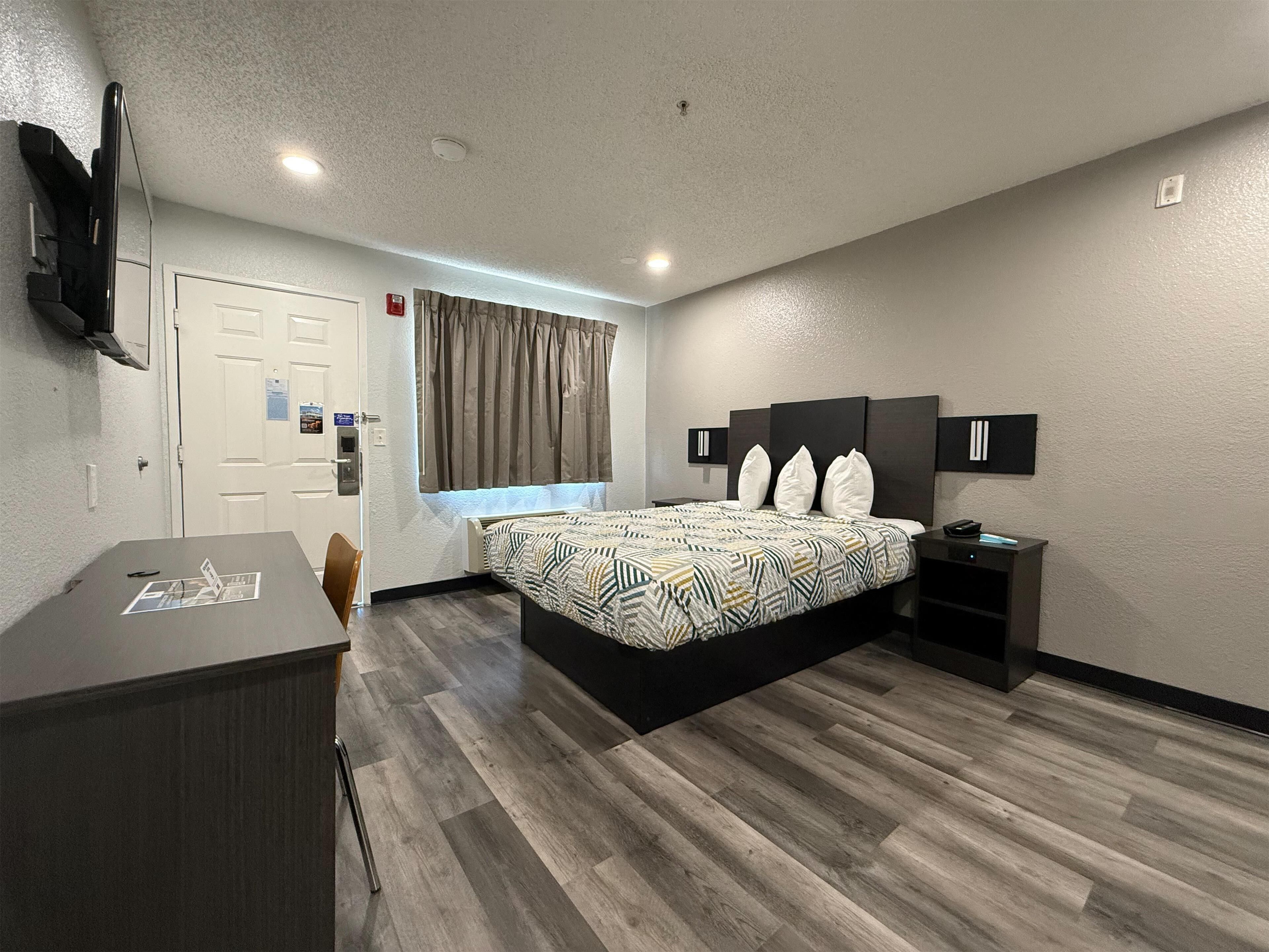 A modern hotel room with a bed, desk, and a TV mounted on the wall.