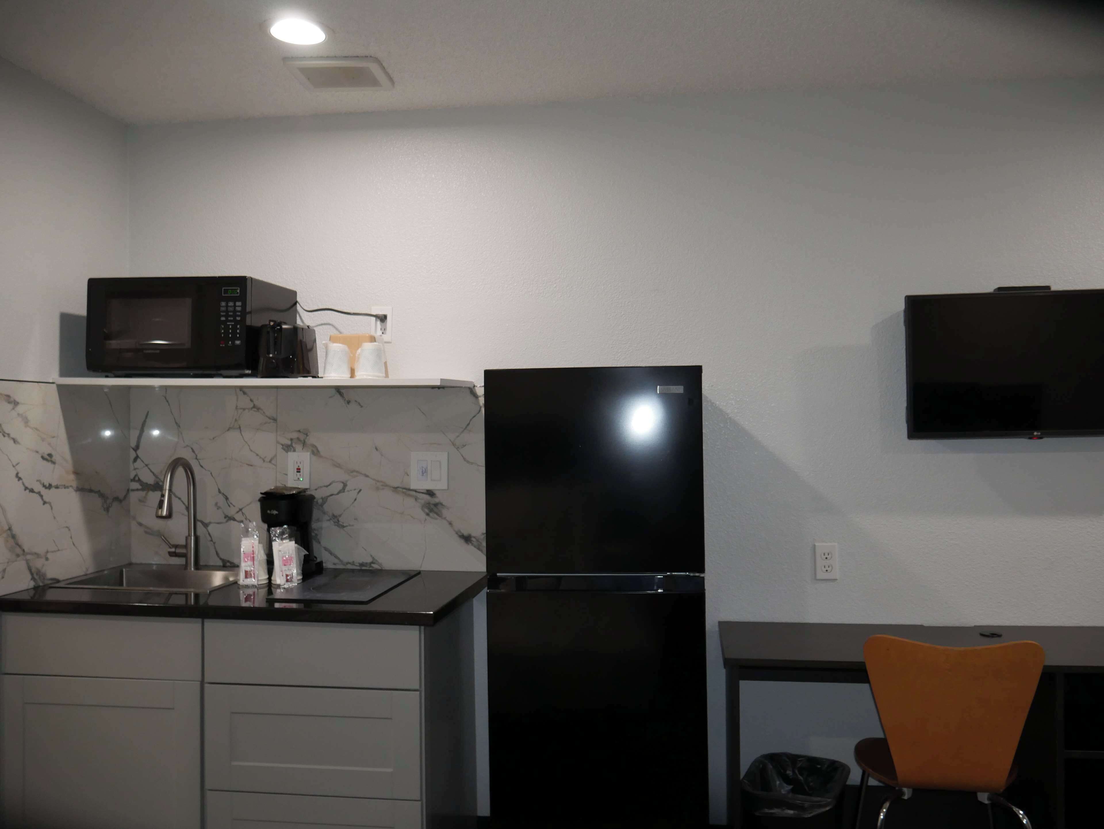Cozinha compacta com micro-ondas, geladeira, pia e uma pequena mesa com uma cadeira.