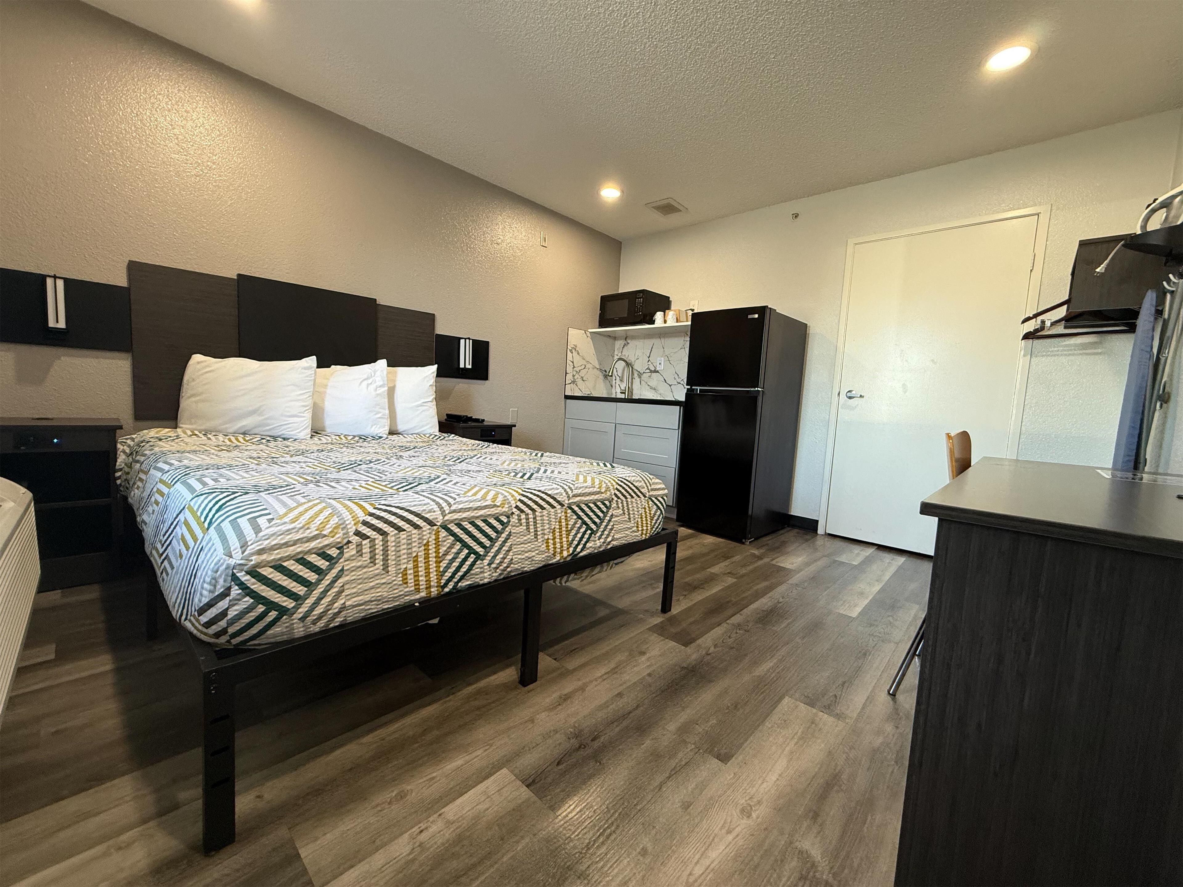 Une chambre d’hôtel compacte comprenant un lit, des tables de chevet, une kitchenette et un petit coin salon.