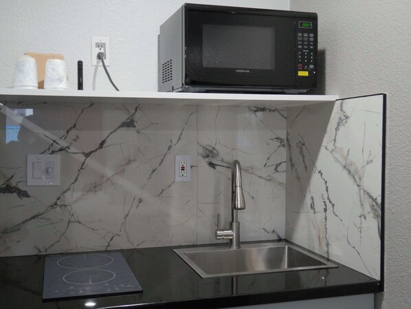 A compact kitchen with a microwave, a sink, and a built-in stovetop.