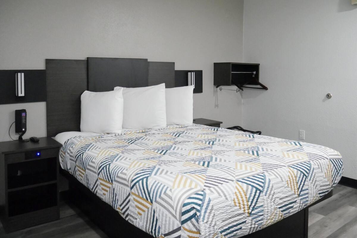 A modern hotel room with a large bed, a bedside table, a nightstand, a wall-mounted shelf, and a power outlet.