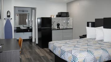A compact hotel room with a bed, a small kitchenette, a desk, and a chair.