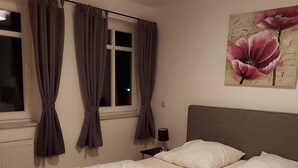 Ein Schlafzimmer mit einem Bett, Vorhängen, einem Nachttisch, einer Lampe und einem Blumenbild.