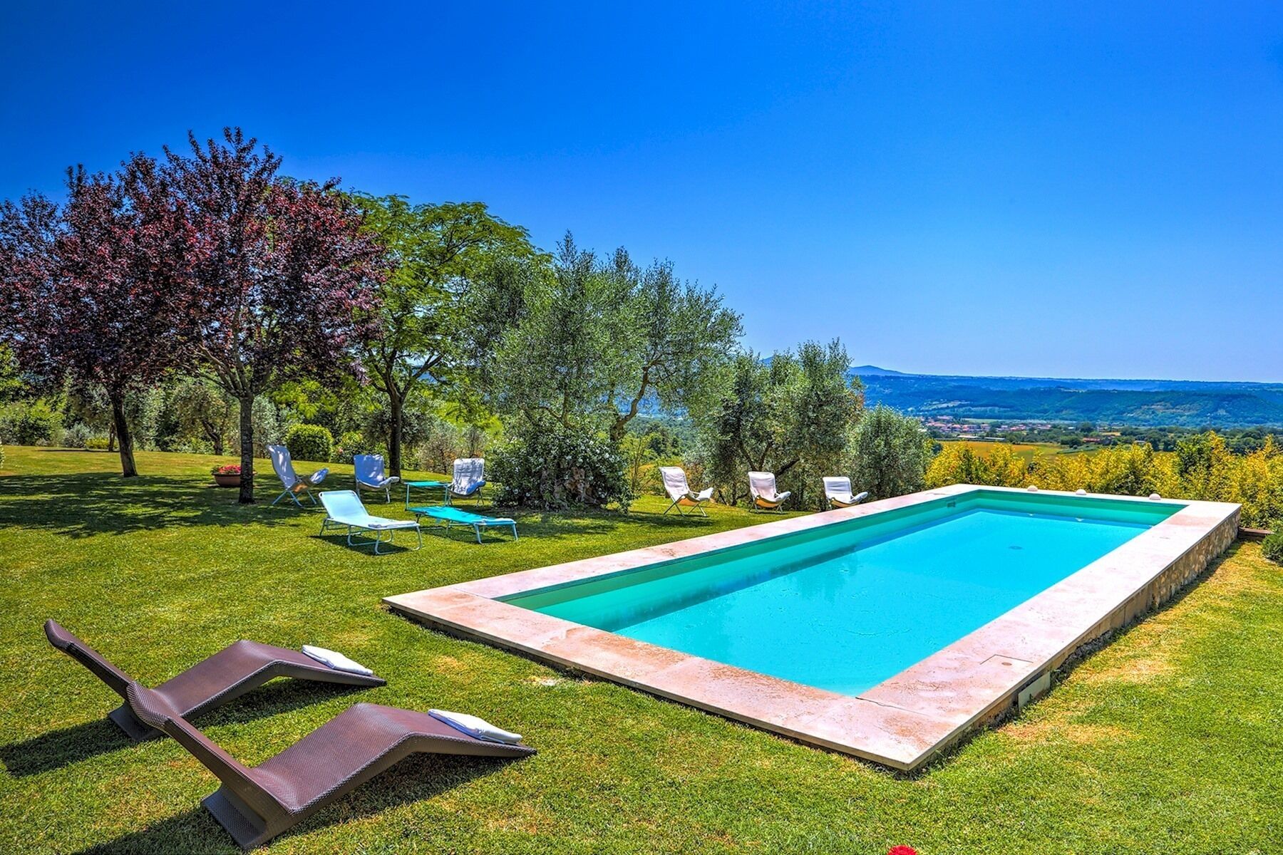 A rectangular swimming pool with a stone edge, surrounded by a well-manicured lawn and several lounge chairs.