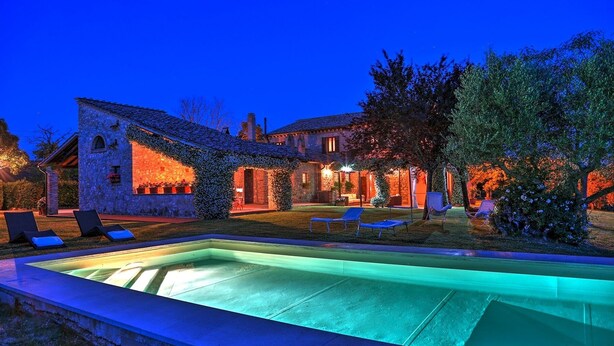 Une villa en pierre dotée d’une piscine, d’un espace extérieur aménagé et d’un jardin bien éclairé au crépuscule.