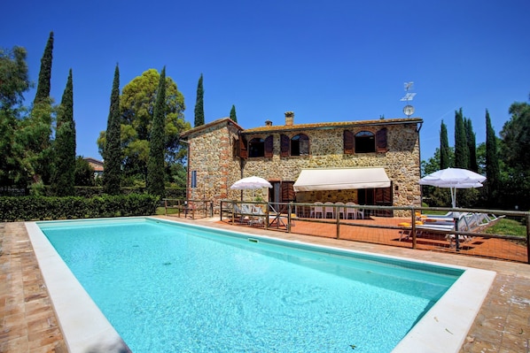Relax by the serene pool surrounded by a traditional stone building and lush greenery.