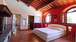 Relax in a traditional room with a large bed, wooden ceiling, and a view of lush greenery.