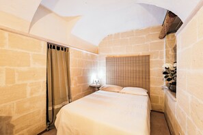 Ein kleines Schlafzimmer mit Steinwänden, einem Einzelbett, einem Nachttisch und einem Fenster mit Vorhängen.