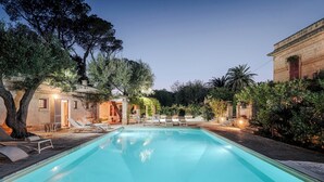 Ein Swimmingpool mit Liegestühlen, ein Steinhaus und Bäume.