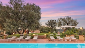 A poolside area with lounge chairs and a view of a lush garden and distant hills. - Casale Ombrone 11, Emma Villas (Campagnatico)
