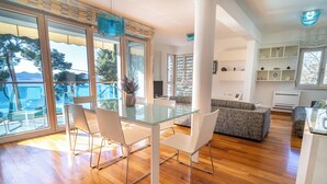 Un salon moderne avec une table à manger en verre, des chaises blanches et un canapé gris.