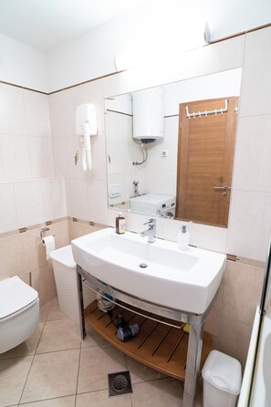 A bathroom with a white sink, a mirror, a wooden door, and a toilet. - Apartment Kolovare (Zadar)