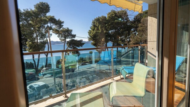 Un balcon doté de rampes en verre, de mobilier d’extérieur et offrant une vue sur la mer et les arbres.