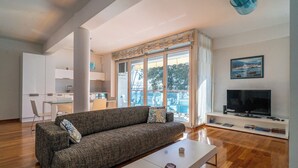 Un salon moderne avec un canapé, une table basse, un téléviseur et une vue sur l’extérieur.