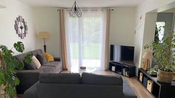 A modern living room with a grey sofa, a flat-screen TV, and a large window with sheer curtains.