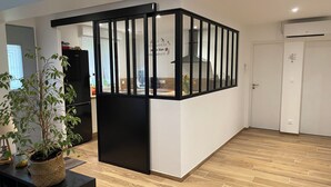 A modern living room with a wooden floor, a black partition, and a potted plant. - Maison l'auvétia 150 m circuit des 24h (Arnage)