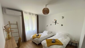 A room with two beds, a wooden desk, a ladder, and a window with sheer curtains. - Maison l'auvétia 150 m circuit des 24h (Arnage)