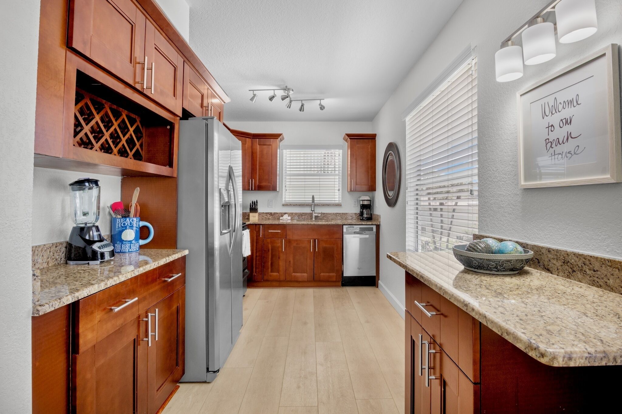 A kitchen with wooden cabinets, a refrigerator, a coffee maker, and a welcome sign.