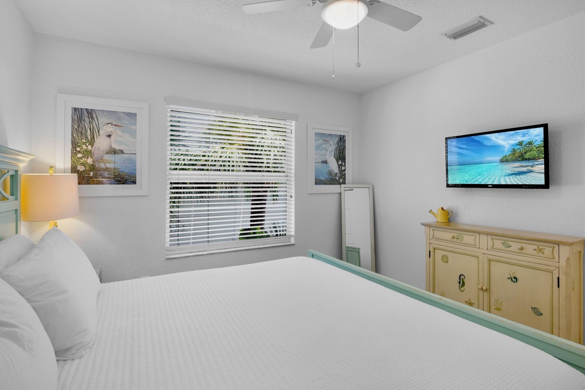 Un dormitorio con cama, televisión, ventana con persianas y un armario.