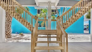 Una escalera de madera que lleva a un edificio azul con palmeras y suelo arenoso.
