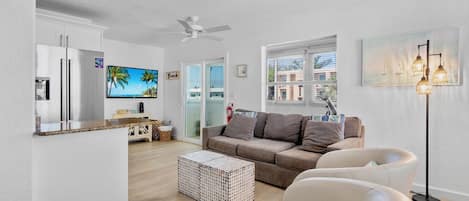 A modern living room with a sofa, chairs, a coffee table, a TV, and a kitchen area with a fridge and microwave.