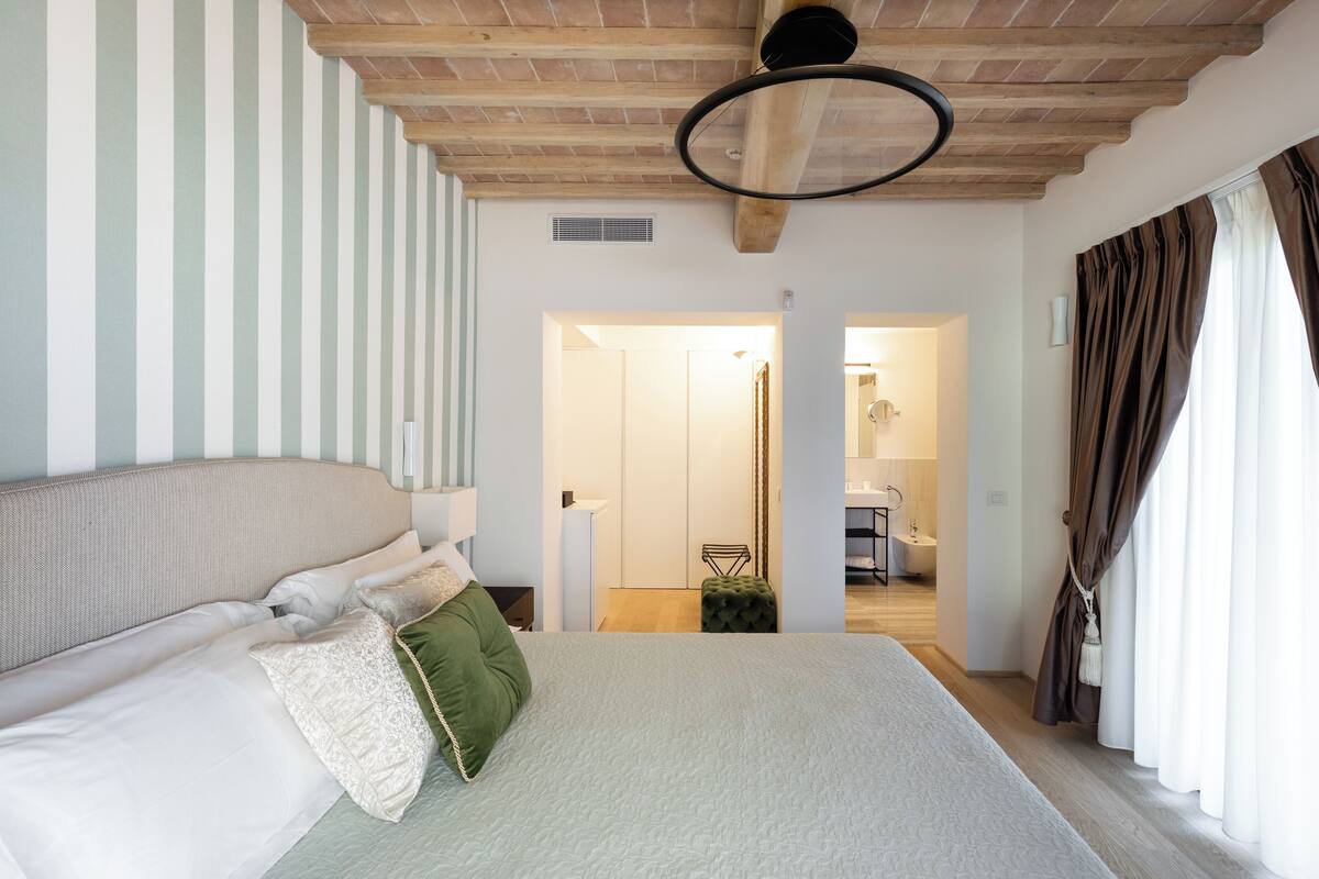 Une chambre à coucher comprenant un lit, une table de chevet, une commode, une fenêtre avec des rideaux et un plafond en bois.