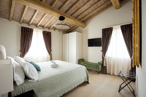 A bedroom with a bed, a green sofa, a TV mounted on the wall, and a ceiling with exposed wooden beams.