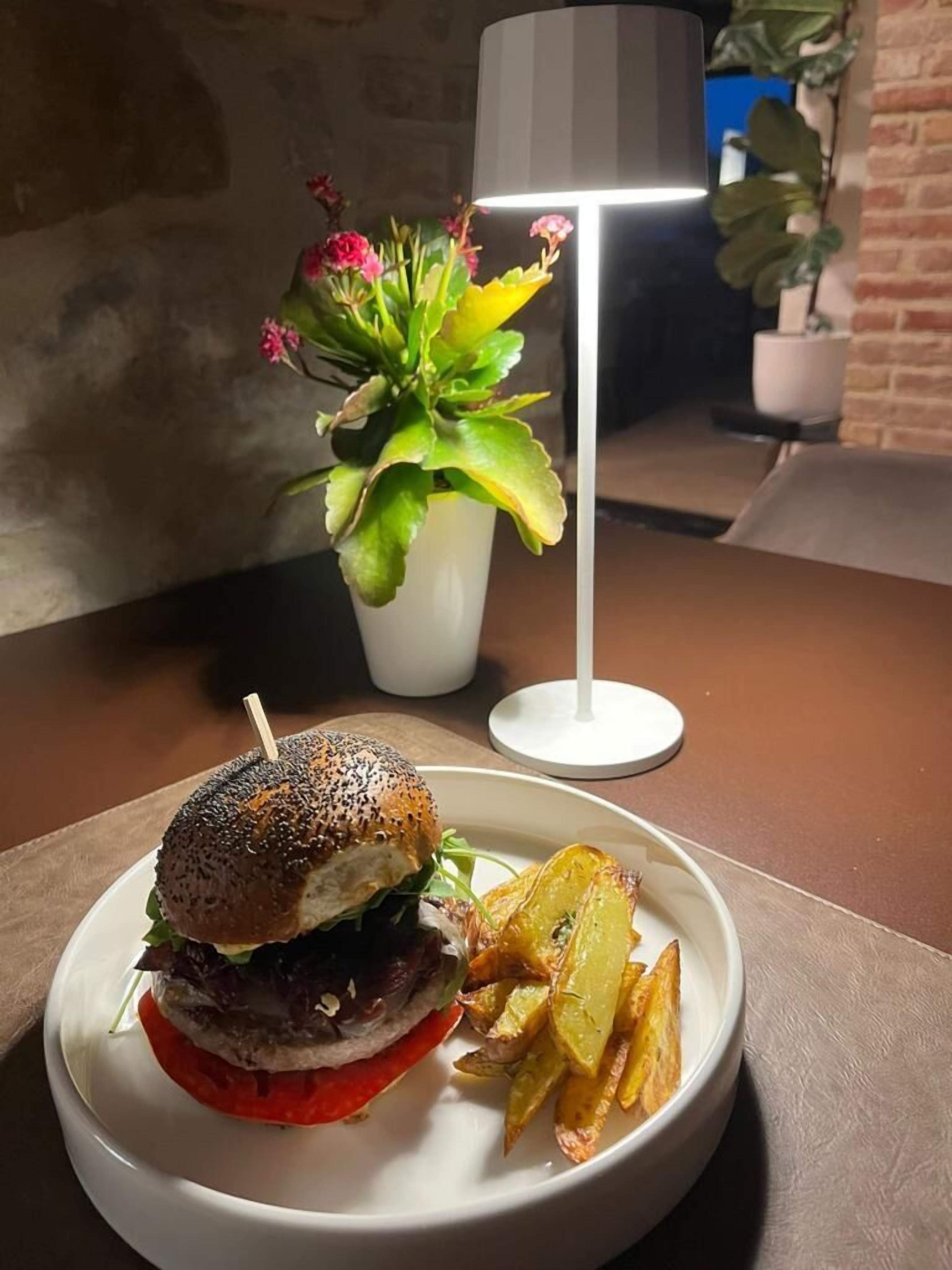 En tallrik med en hamburgare och pommes frites på ett bord, en lampa och en krukväxt i bakgrunden.