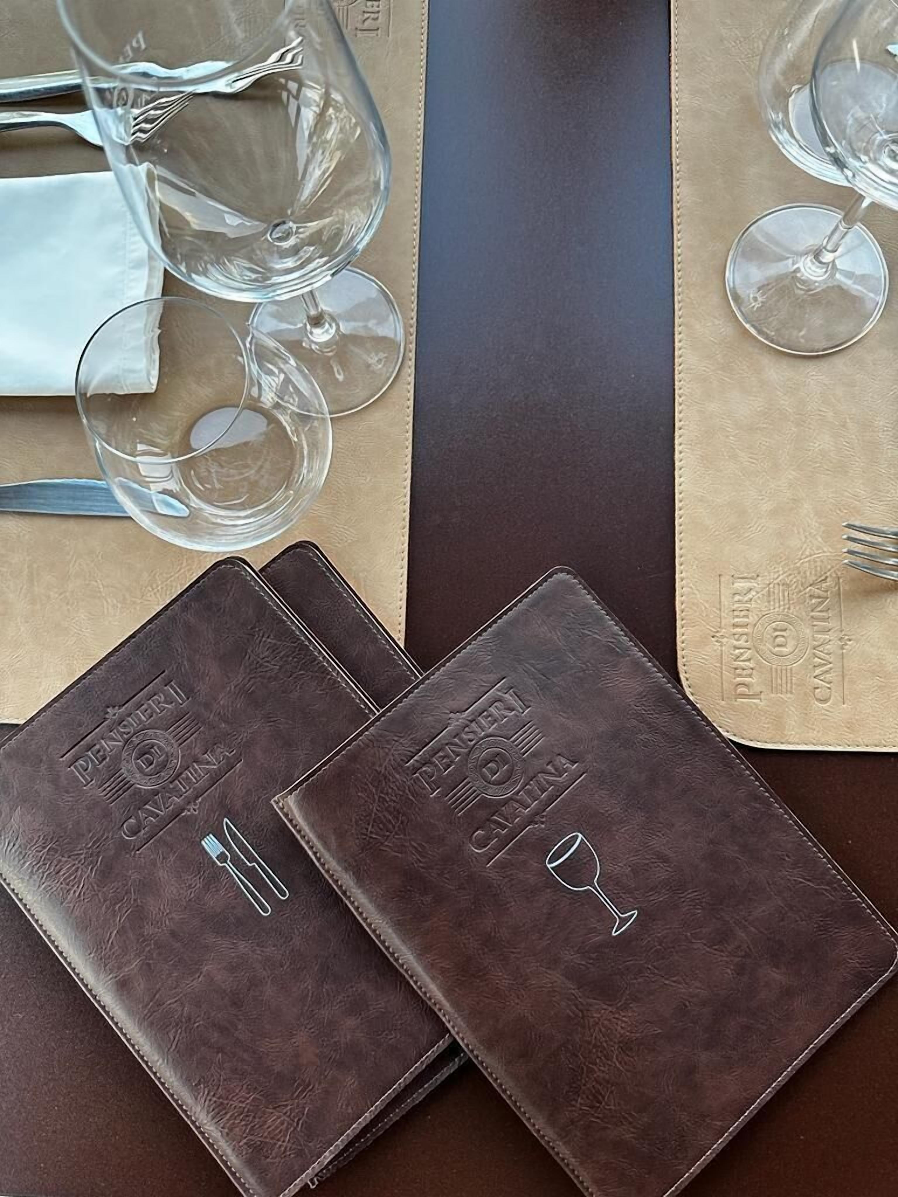 A table set with wine glasses, cutlery, and two leather-bound notebooks with embossed text.