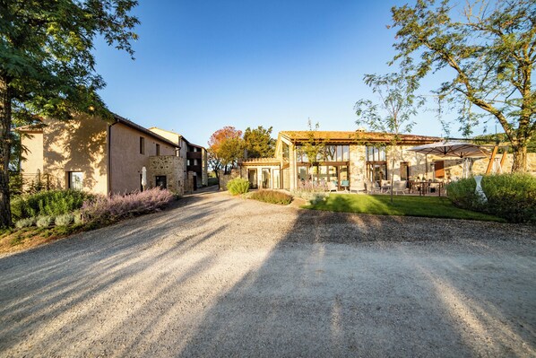 A gravel driveway leading to a building with a stone facade and a glass extension.