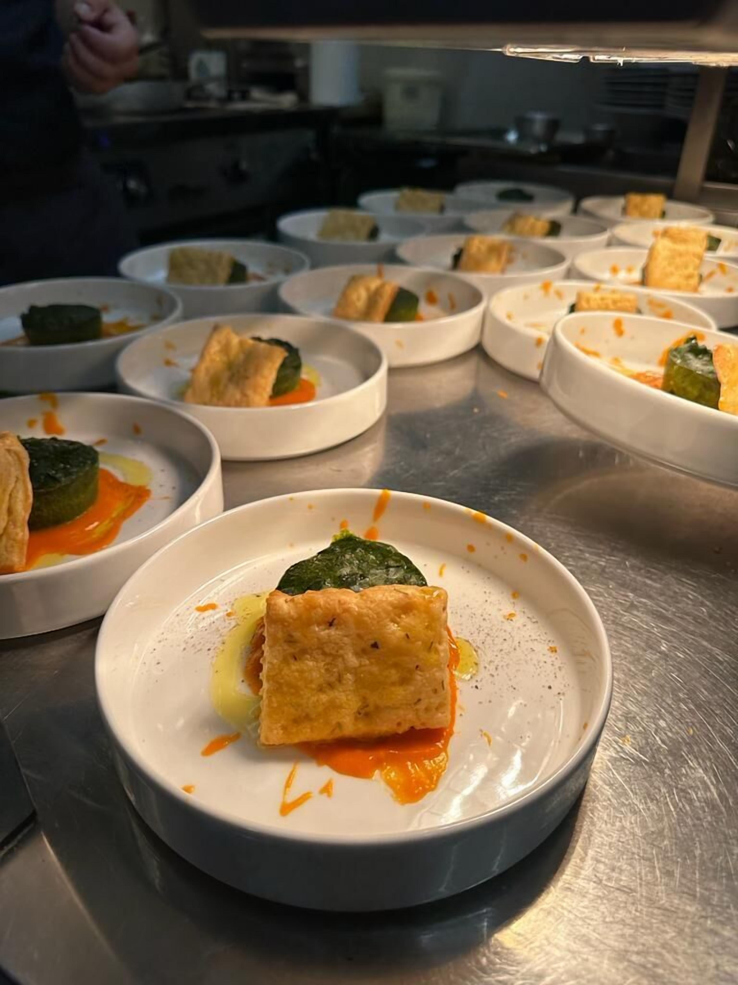 Una serie de platos blancos con comida, dispuestos sobre una encimera de acero inoxidable.