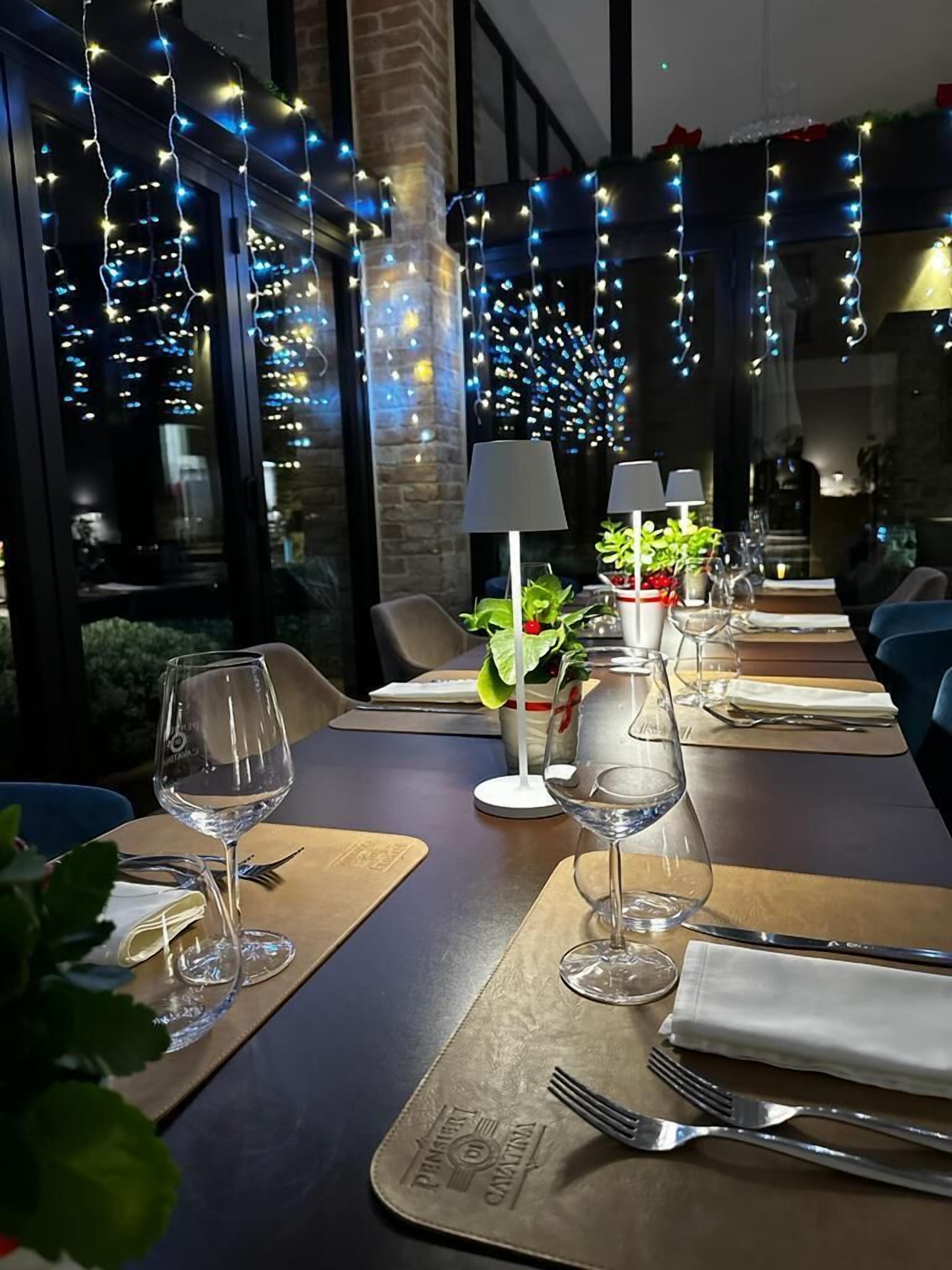 A restaurant setting with tables set for dining, string lights, and potted plants.