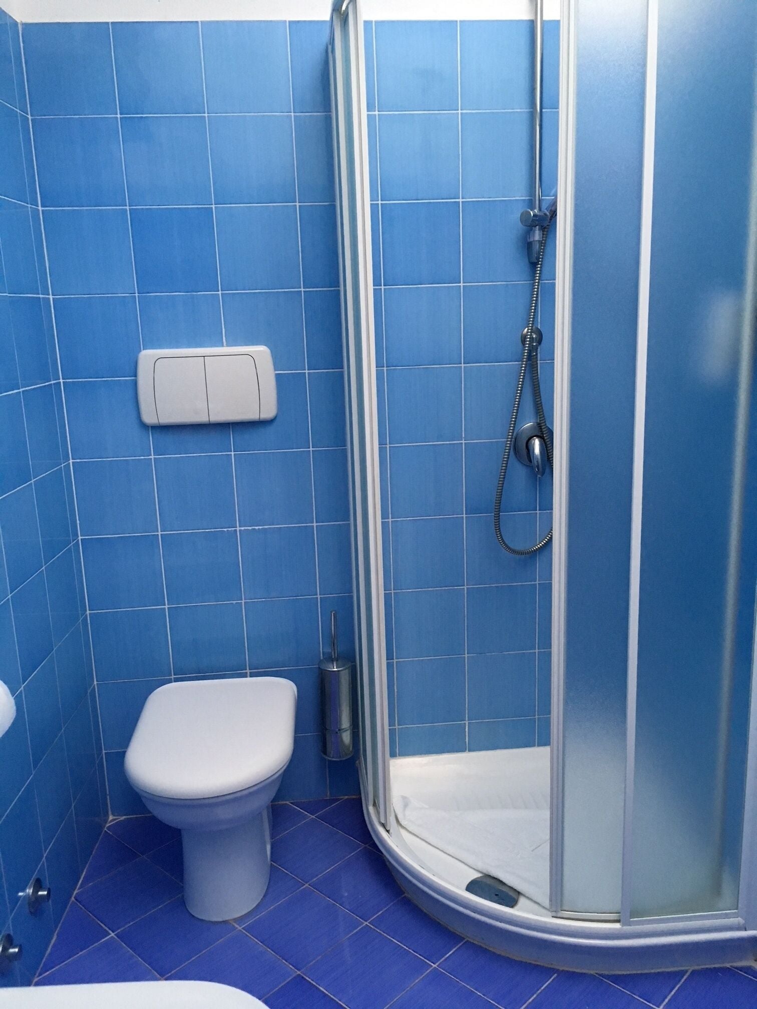 Un baño con inodoro, ducha con puerta de cristal y azulejos azules en paredes y suelo.