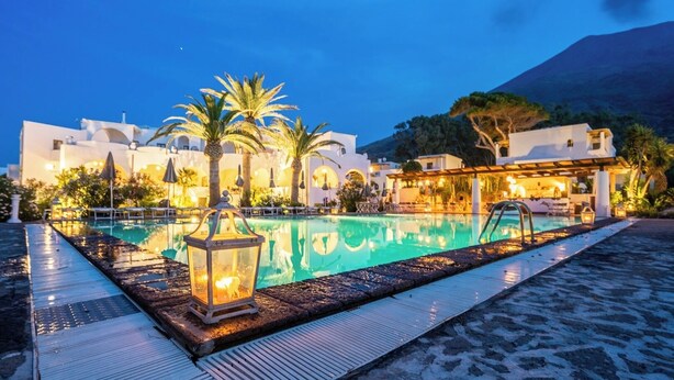 A poolside area with a clear pool, palm trees, and a building with white architecture. - La Sciara Resort Hotel (Lipari)