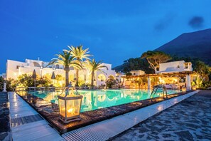 A poolside area with a clear pool, palm trees, and a building with white architecture. - La Sciara Resort Hotel (Lipari)