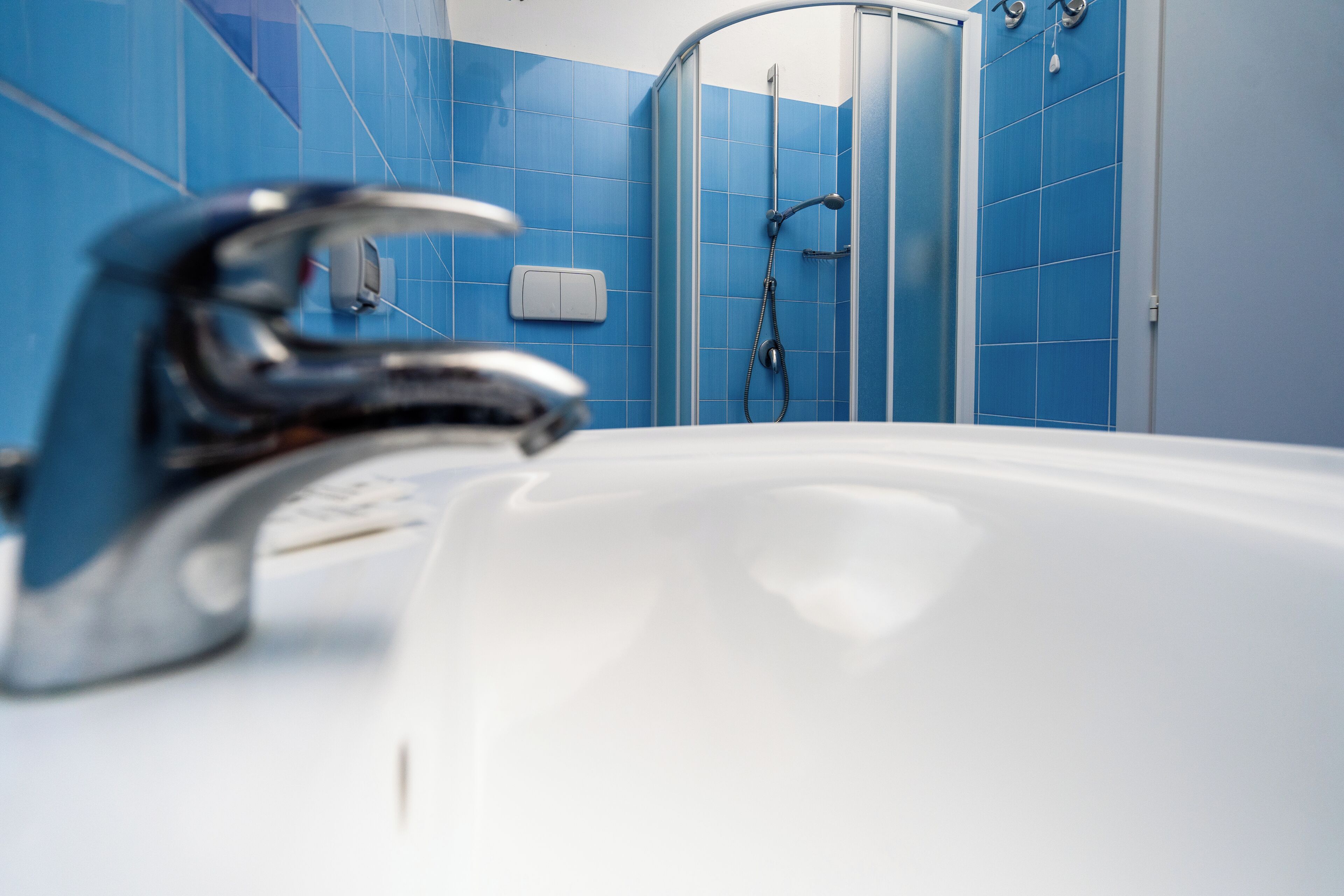 Ein Badezimmer mit einem weißen Waschbecken, blauen Fliesen und einer Duschkabine.