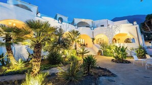 A white building with multiple arches and a courtyard with palm trees and plants. - La Sciara Resort Hotel (Lipari)