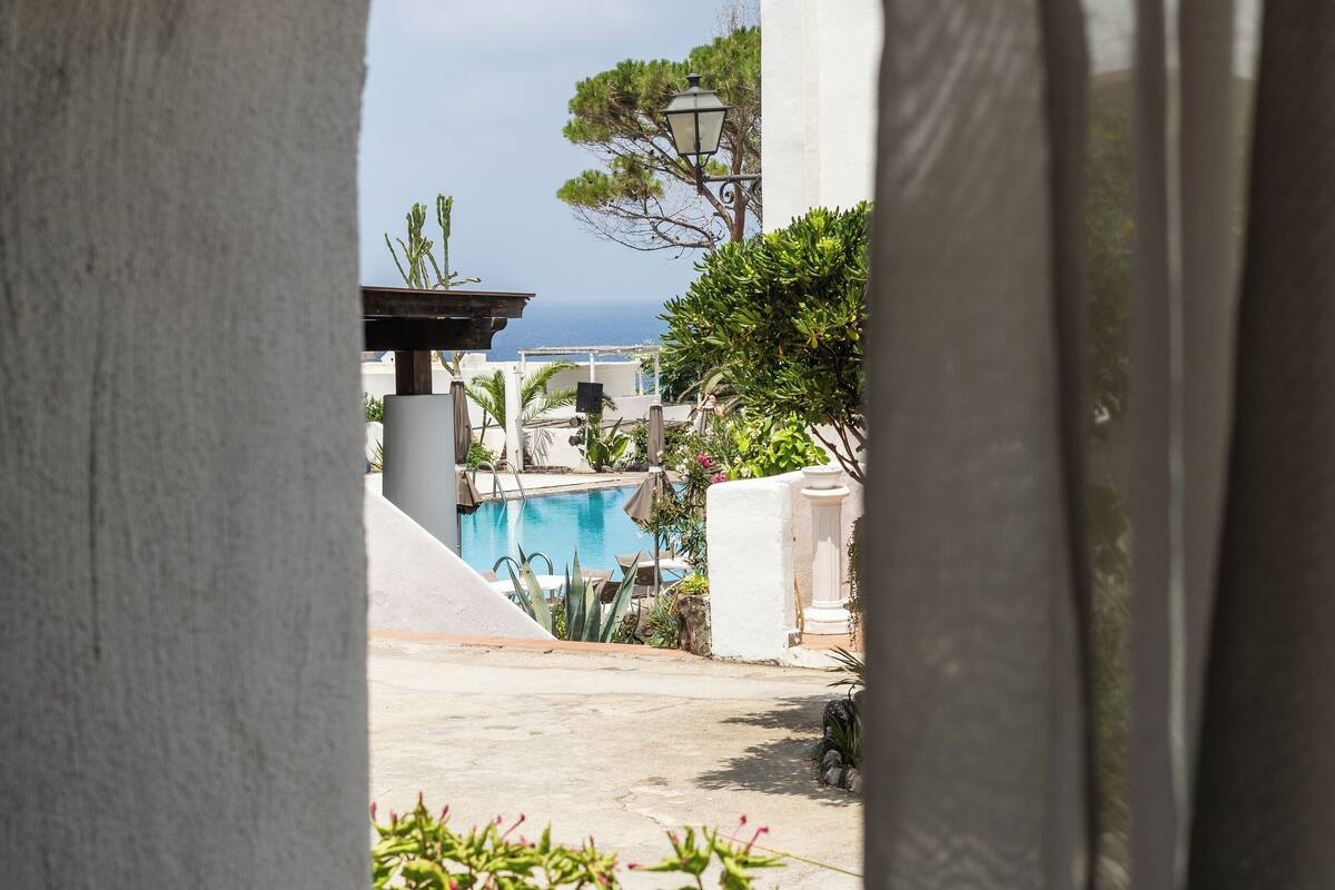 A view through an archway of a pool area with a clear sky and a building in the background.