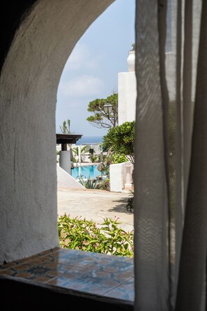 Blick durch einen Bogen auf einen Poolbereich mit blauem Himmel und einem Gebäude im Hintergrund.