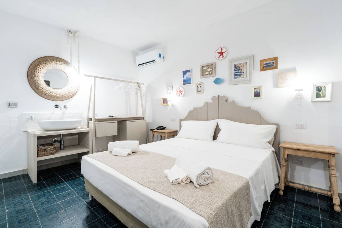 A hotel room with a large bed, a round mirror, a sink, and a wooden nightstand.