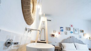 A bathroom with a large white basin, a wooden ladder, a bed with white bedding, and wall-mounted lights. - La Sciara Resort Hotel (Lipari)