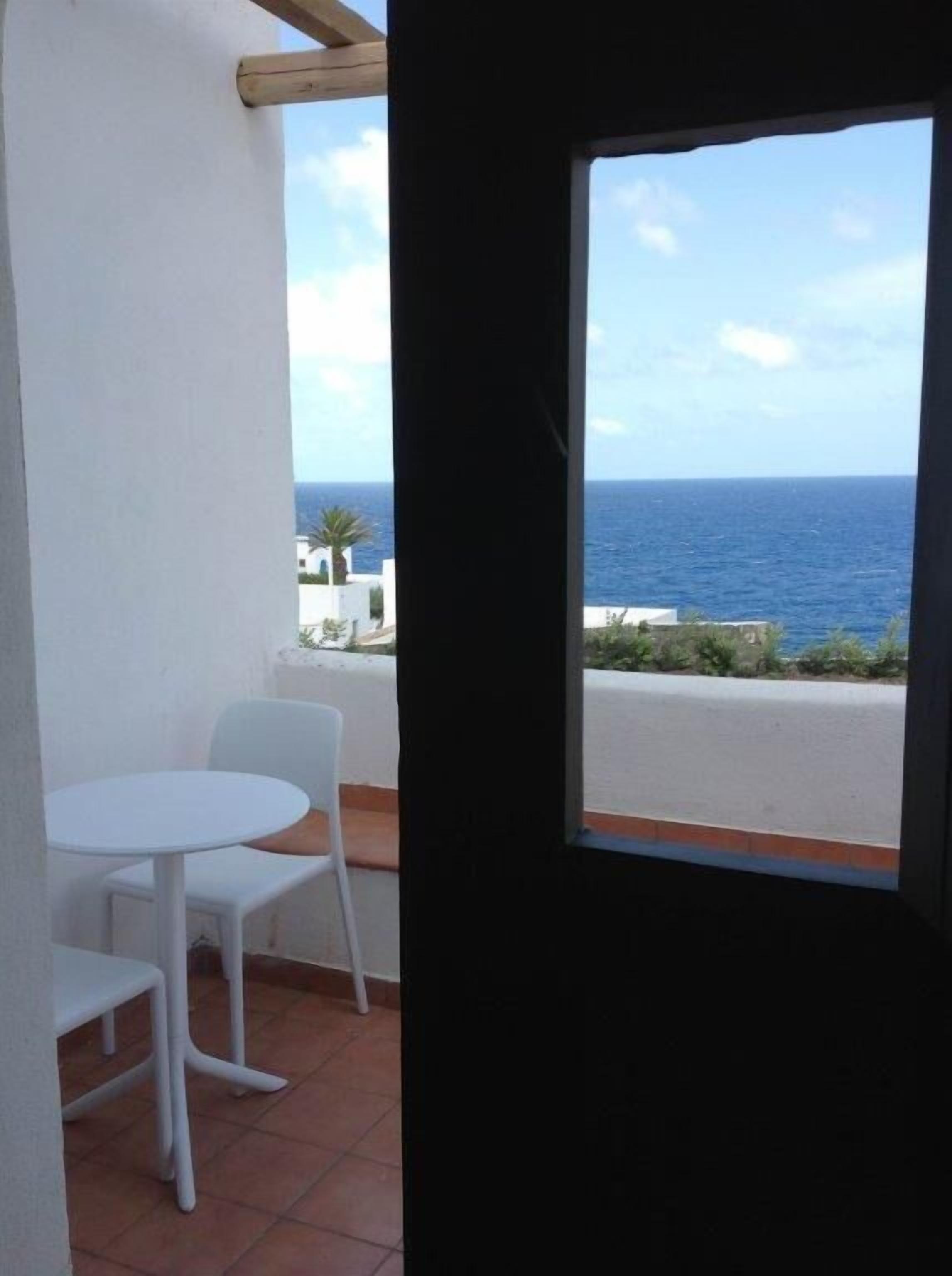 A balcony with a white table and chairs, a view of the sea, and a clear sky.