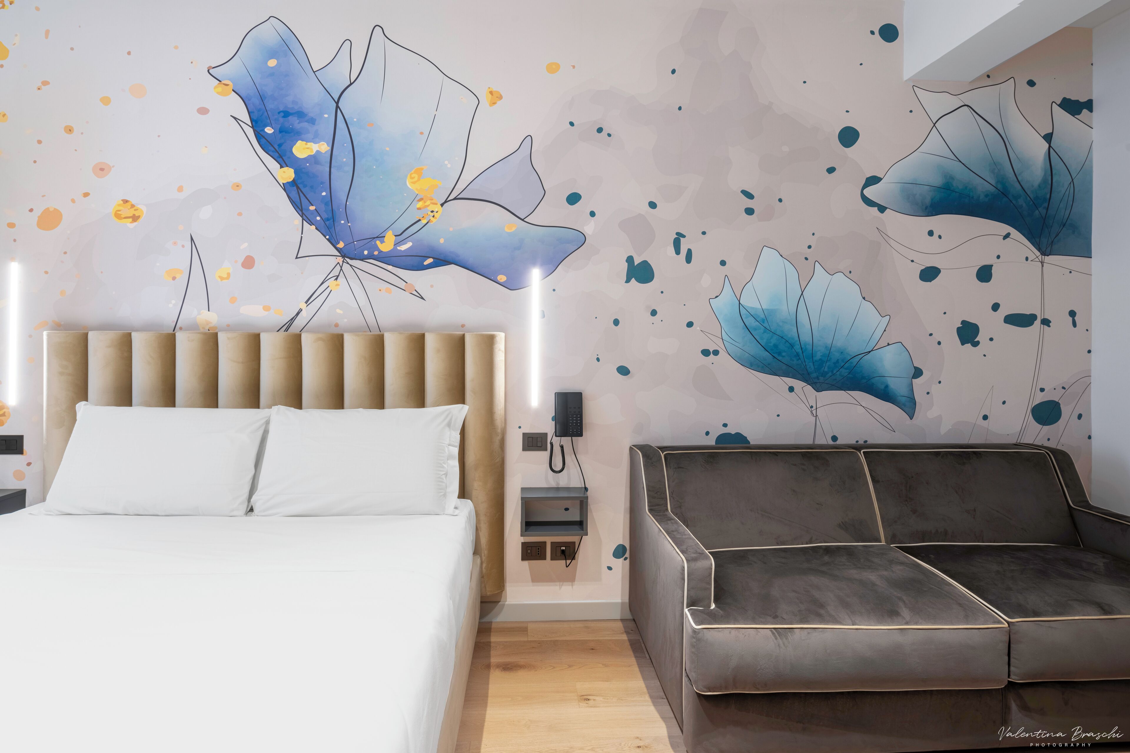 A modern bedroom with a bed, a grey sofa, and abstract wall art.